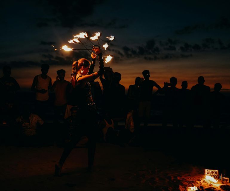 Un artista del fuoco si esibisce su una spiaggia al tramonto per un gruppo WeRoad in silhouette.