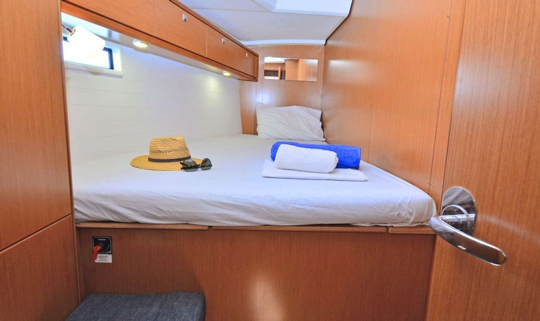 Das Innere einer kompakten Bootskabine mit einem gemachten Bett, Strohhut, Sonnenbrille und ordentlich gefalteten Handtüchern.