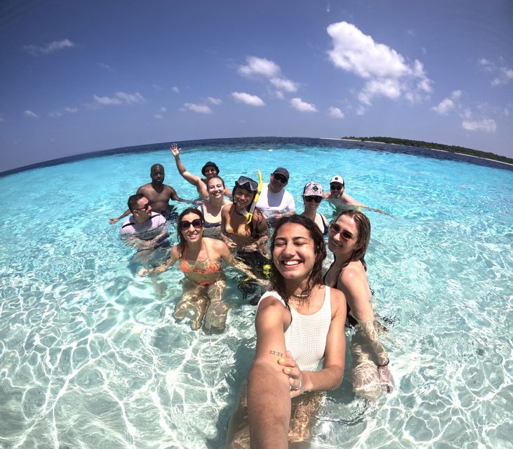 Un groupe WeRoad prend un selfie en nageant ensemble dans une eau océanique turquoise claire par une journée ensoleillée.