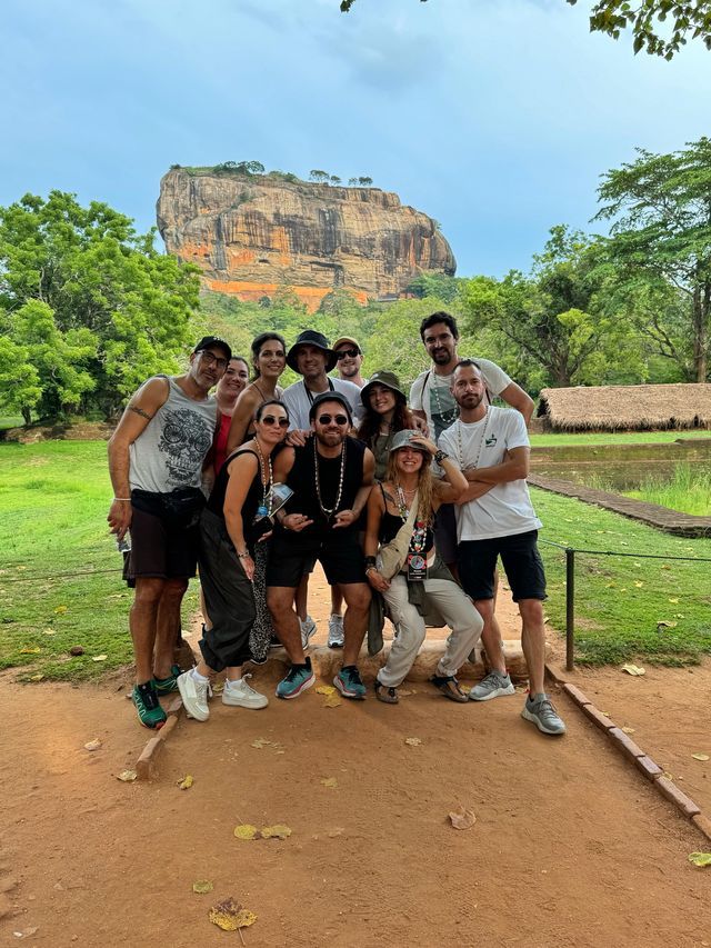 Un gruppo WeRoad in viaggio si ferma per una foto su un sentiero sterrato, davanti a una grande formazione rocciosa immersa nel verde lussureggiante.