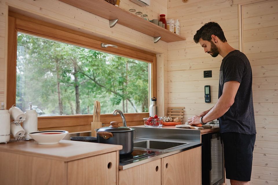 Un uomo taglia le verdure su un tagliere in una cucina in legno con una grande finestra che si affaccia su una foresta
