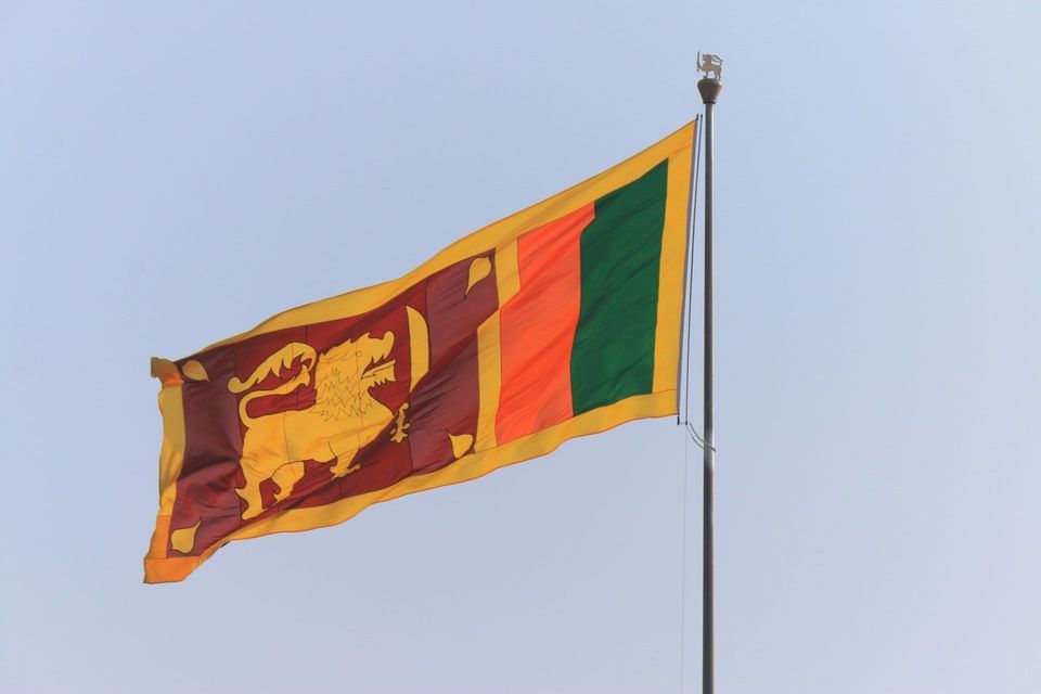 La bandiera nazionale dello Sri Lanka, con un leone d'oro, che sventola su un'asta contro un cielo azzurro chiaro.