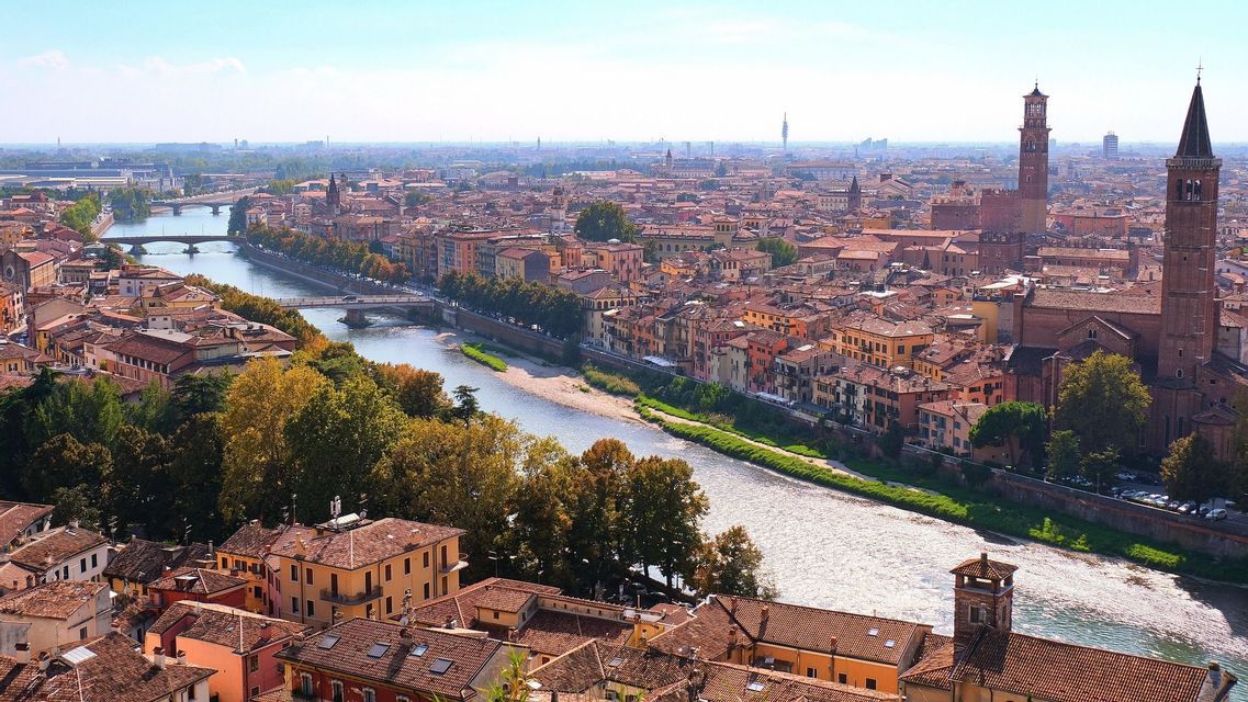 Una vista aérea de una ciudad con un río serpenteante, puentes y edificios de tejados rojos bajo un cielo azul claro.