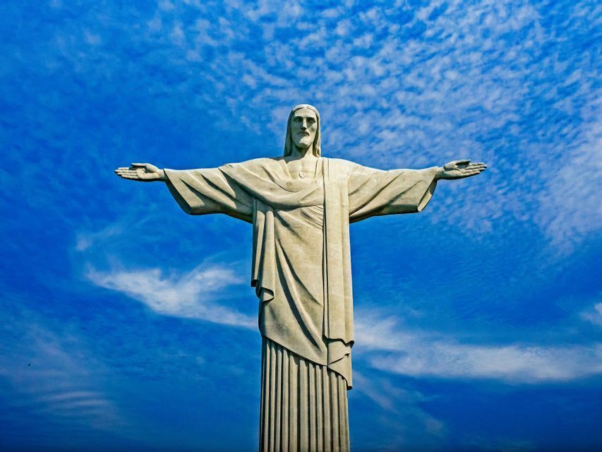 The Christ the Redeemer statue seen from below, with its arms outstretched against a deep blue sky with scattered clouds.