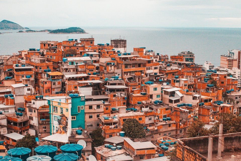Densely packed orange brick buildings with blue water tanks on a hillside overlooking the ocean and distant islands.