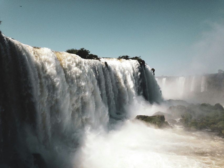 A wide, powerful waterfall cascades over a rocky cliff, sending up a thick cloud of mist from the basin below.