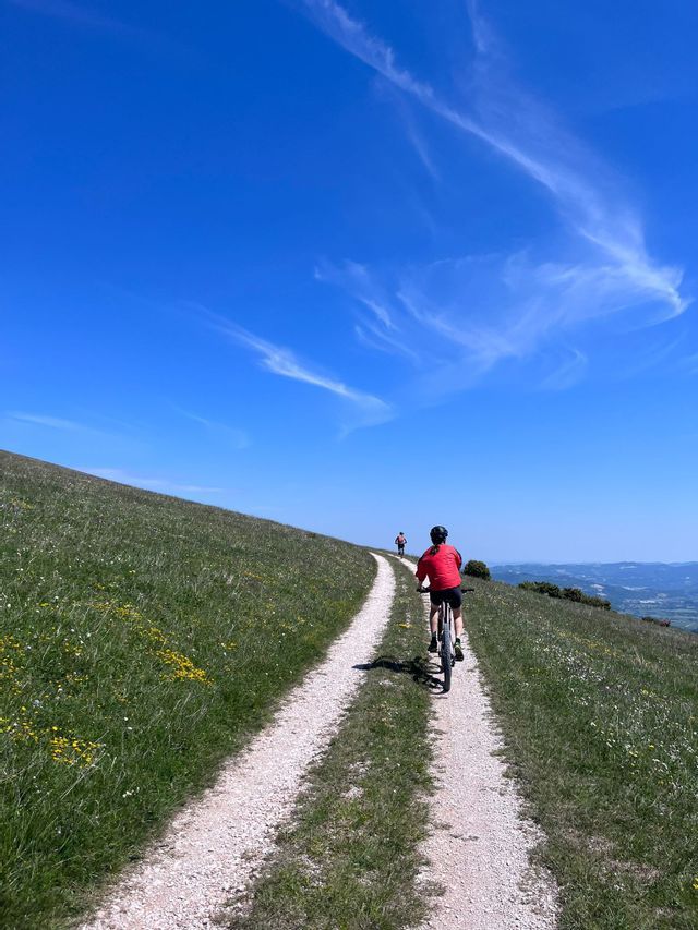 Un viaggio di gruppo WeRoad in bici su un sentiero sterrato, su per una collina erbosa, sotto un cielo azzurro brillante con nuvole leggere.