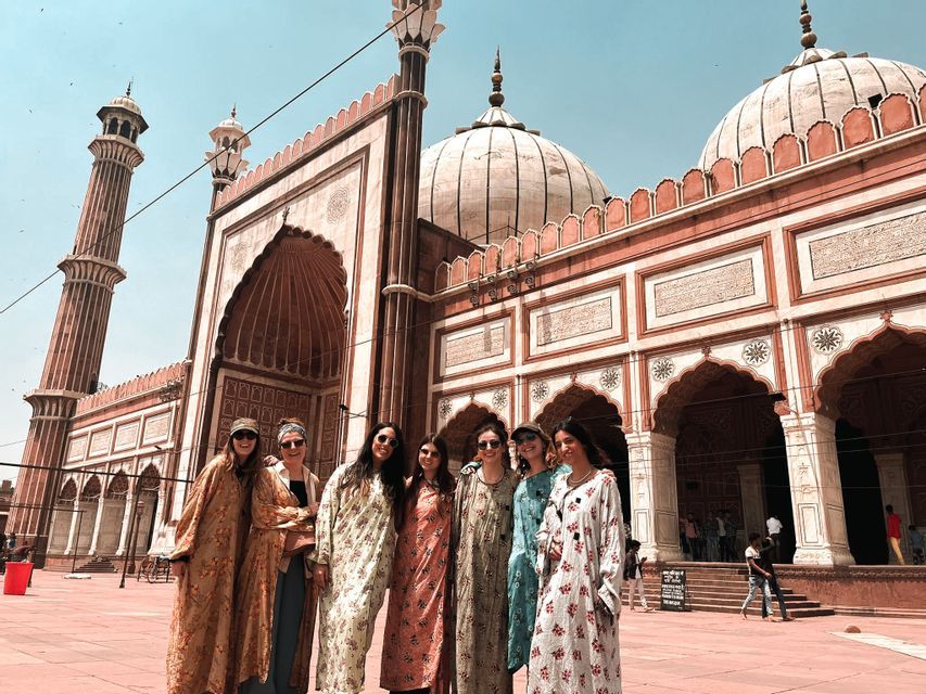 Eine WeRoad-Gruppenreise von sieben Frauen posiert in einem Innenhof vor einer großen roten Sandsteinmoschee mit weißen Kuppeln.