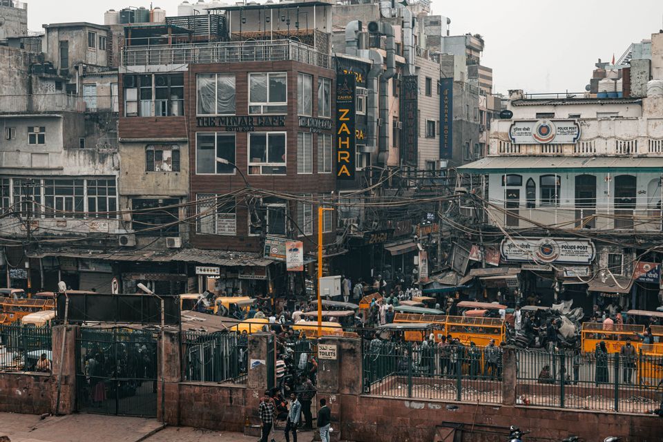 Ein erhöhter Blick auf eine belebte Stadtstraße voller Fußgänger, gelber Autorikschas und dichter, verwitterter Gebäude.