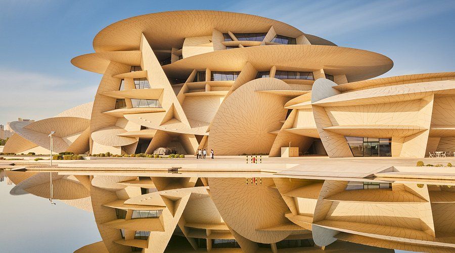 Un grande edificio moderno con architettura a strati, a forma di disco, si riflette nell'acqua calma mentre alcune persone stanno nelle vicinanze.