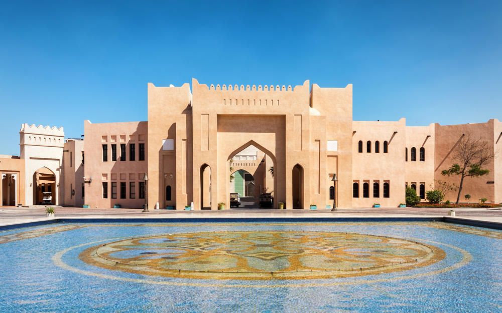 Un edificio color sabbia con archi tradizionali si erge dietro una fontana rotonda decorata con piastrelle a mosaico blu e oro.