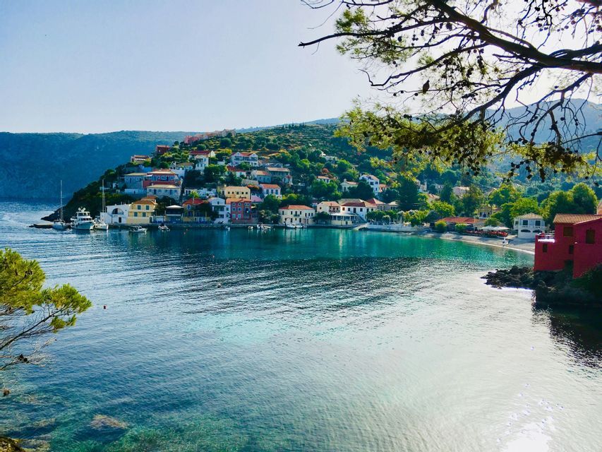 Un colorato villaggio sul mare su una lussureggiante collina verde si affaccia su una baia calma con acqua cristallina turchese e barche.