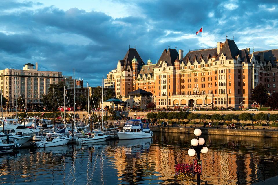 Ein prächtiges Hotel an einer Stadtpromenade mit im Hafen liegenden Booten bei einem dramatischen Sonnenuntergang.