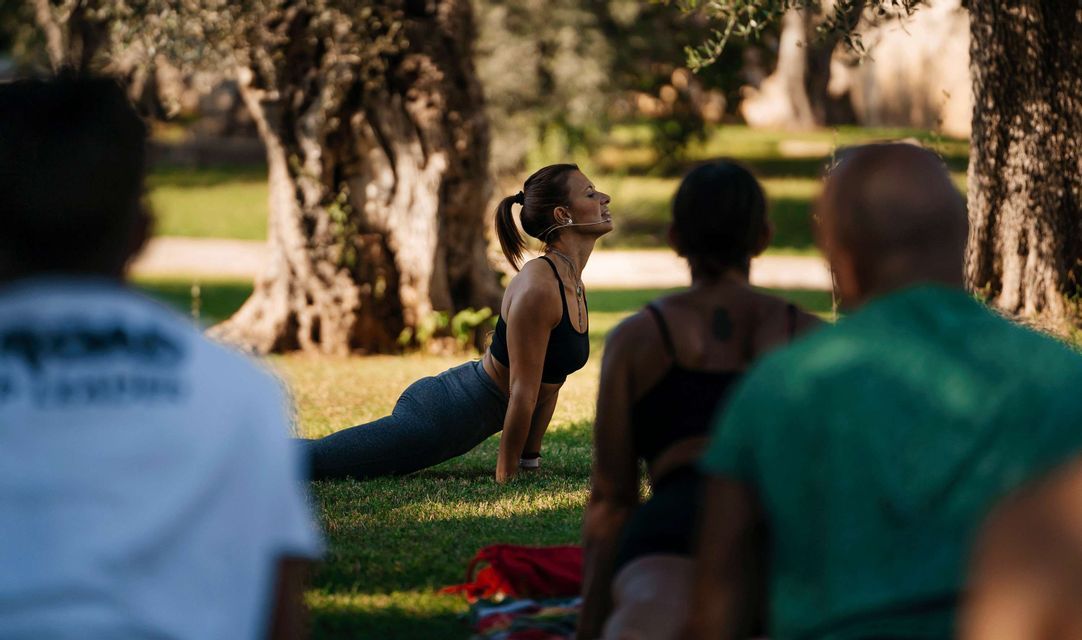 Un istruttore di yoga con microfono guida un gruppo WeRoad in una posa yoga su un prato erboso.
