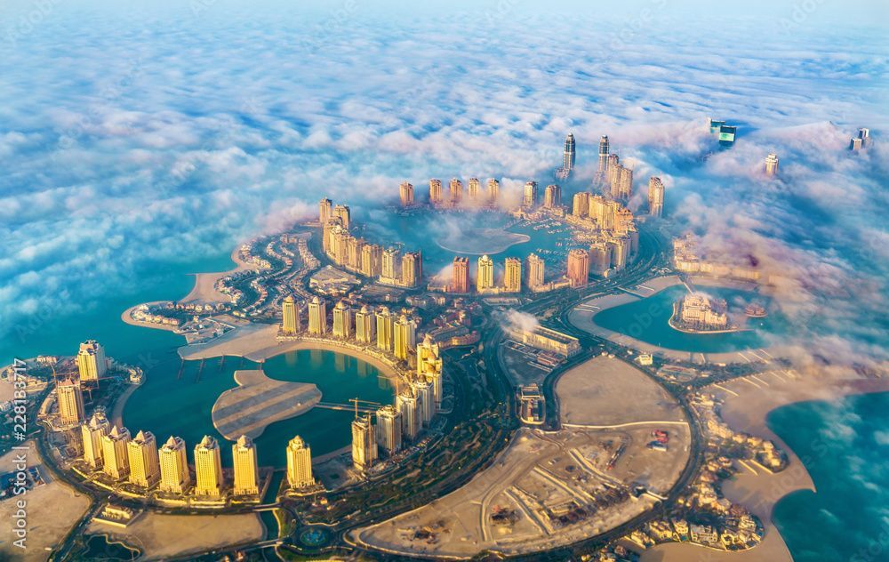 Vista aerea di una moderna città costruita su un arcipelago artificiale, con grattacieli circondati da acqua turchese e nuvole.
