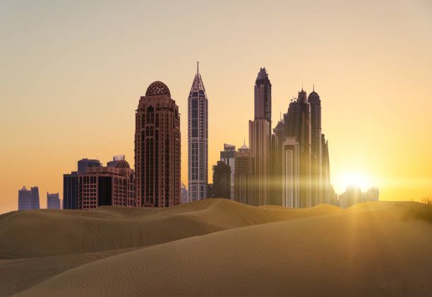 Uno skyline moderno di grattacieli che si ergono da vaste dune di sabbia desertiche durante un tramonto dorato.