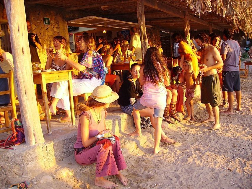 Un viaje en grupo de WeRoad socializando en un chiringuito rústico en la arena, bañado por la luz dorada del atardecer.