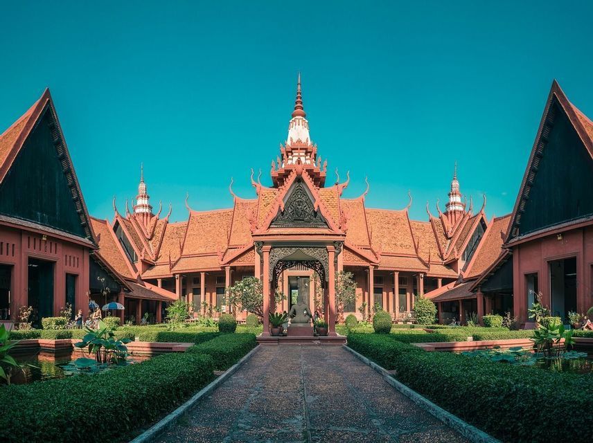 Une vue symétrique d'un complexe de temples rouges avec un chemin de pierre traversant une cour verte sous un ciel bleu clair.