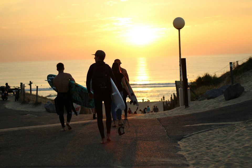 Un viaggio di gruppo WeRoad di surfisti in muta che portano le loro tavole lungo un sentiero verso l'oceano al tramonto.