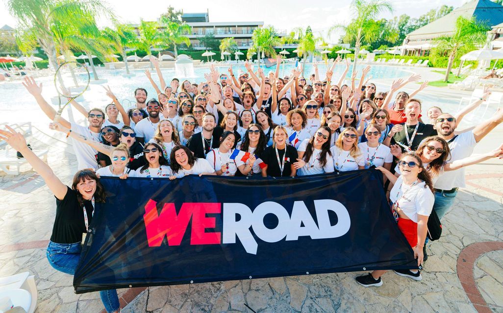 Un grande gruppo WeRoad in viaggio che posa ed esulta per una foto con uno striscione davanti a una piscina.