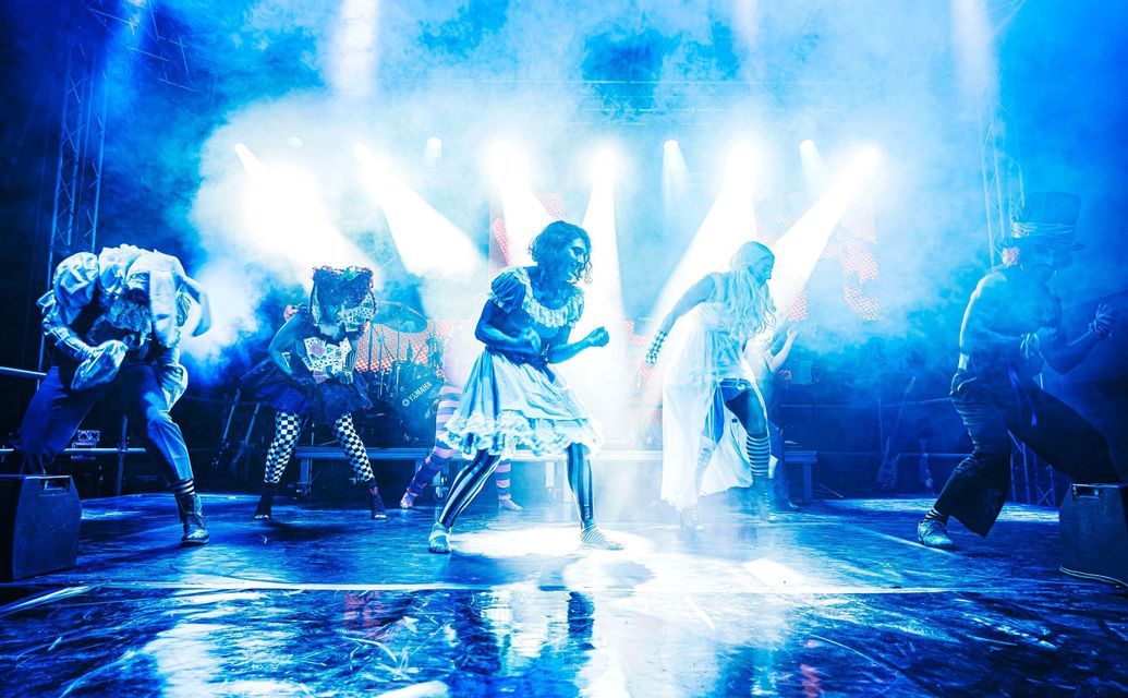 Un gruppo di artisti in costumi fantasy balla su un palco illuminato da luci blu e avvolto da fumo scenico.