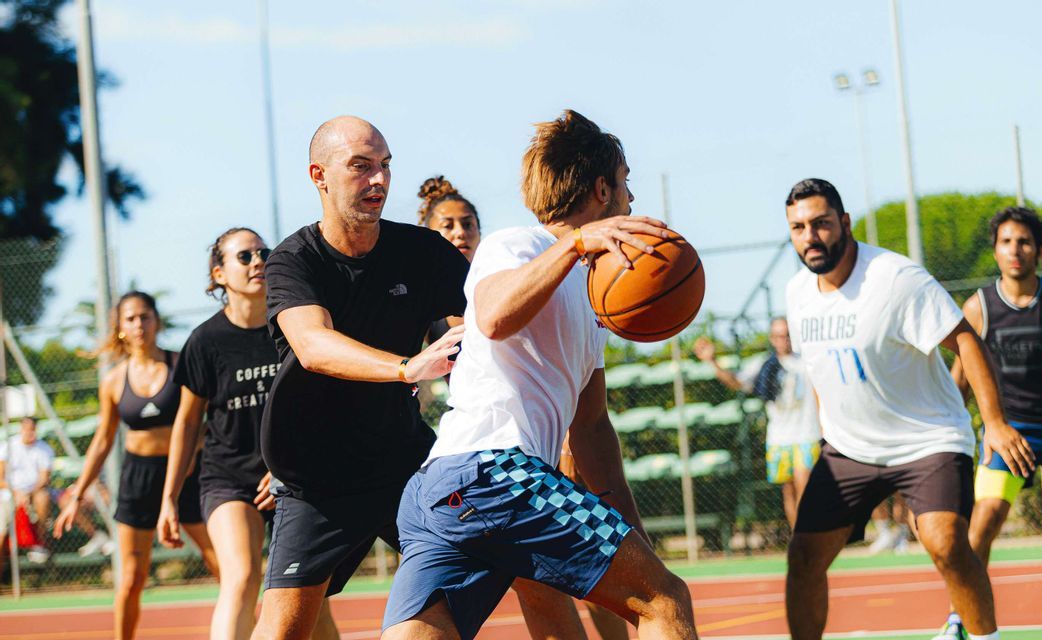Un viaggio di gruppo WeRoad giocando a basket su un campo all'aperto sotto il sole splendente.
