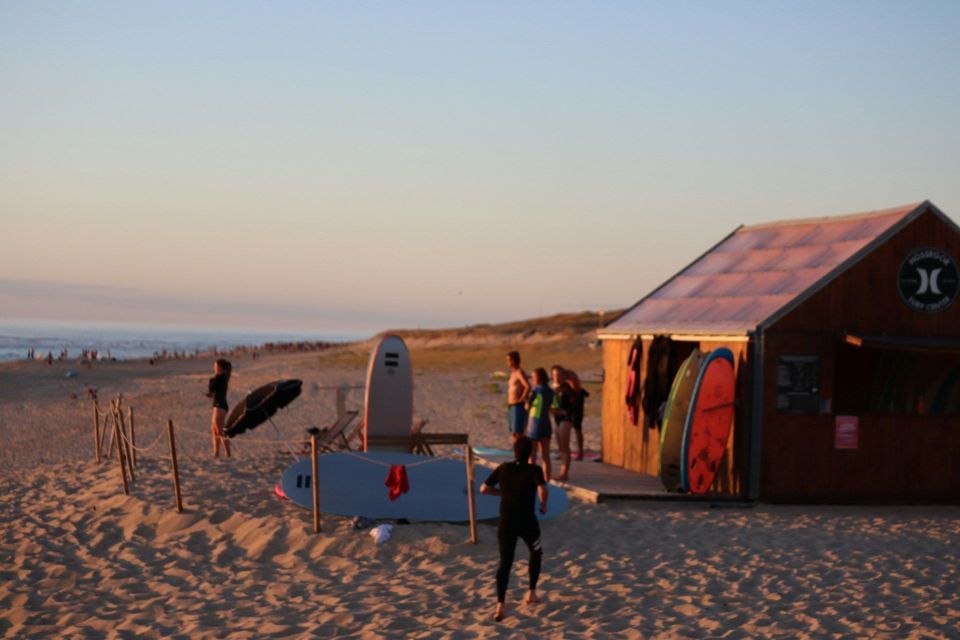 Un viaggio di gruppo WeRoad che si rilassa su una spiaggia sabbiosa al tramonto, con tavole da surf appoggiate a una capanna di legno.