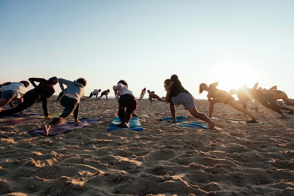 Un viaggio di gruppo WeRoad che pratica posizioni yoga all'unisono su tappetini posizionati su una spiaggia sabbiosa all'alba.