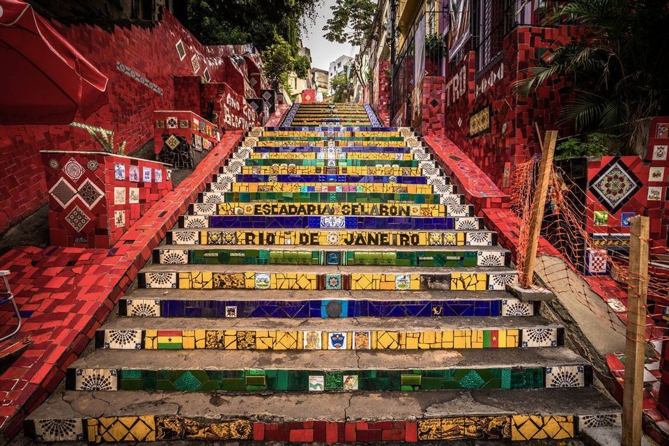 The mosaic-covered steps of the Escadaria Selarón in Rio de Janeiro, flanked by bright red tiled walls.