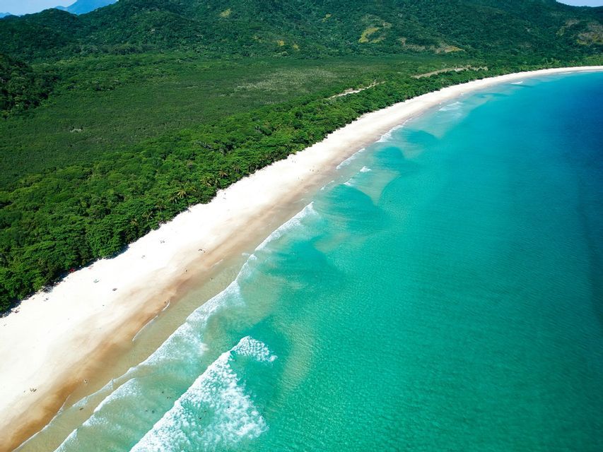 Aerial view of a long, curving white sand beach bordered by turquoise ocean waters and a lush green forest.