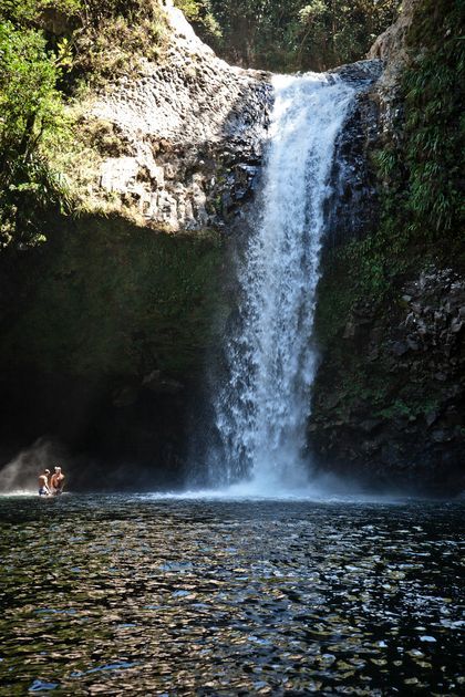Un voyage de groupe WeRoad se baignant dans l'eau au pied d'une grande cascade qui dévale une falaise rocheuse escarpée.
