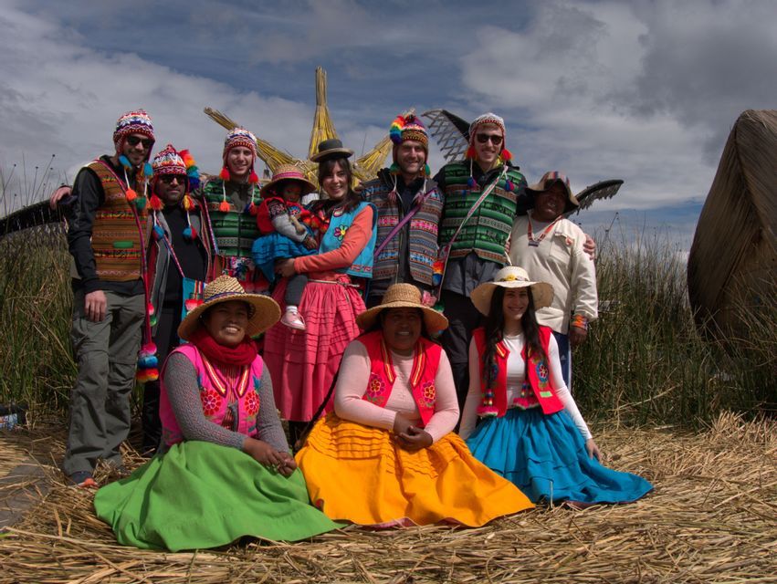 Eine WeRoad Gruppenreise posiert für ein Foto mit Einheimischen in farbenfroher traditioneller Kleidung auf einem Schilfbett.