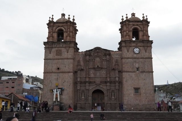 Eine große, reich verzierte Steinkirche mit zwei Glockentürmen steht auf einem öffentlichen Platz mit Menschen auf ihren Stufen.