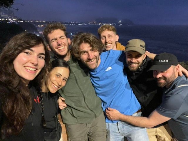 Eine WeRoad-Gruppenreise mit lachenden Freunden, die nachts ein Gruppen-Selfie aufnehmen, mit Blick auf eine beleuchtete Küste.