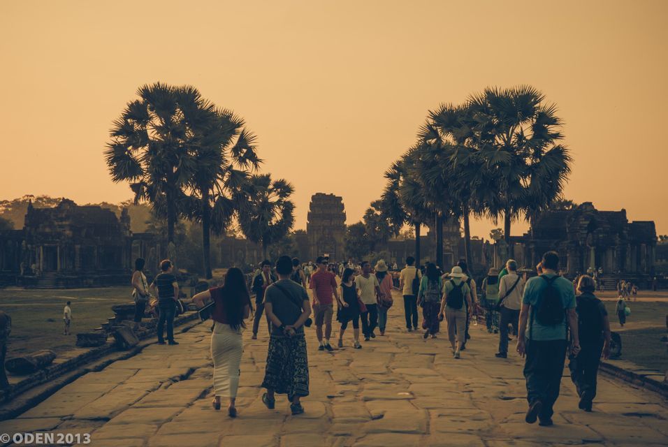 Un voyage de groupe WeRoad emprunte une chaussée de pierre vers d'anciens temples entourés de palmiers sous un ciel doré.