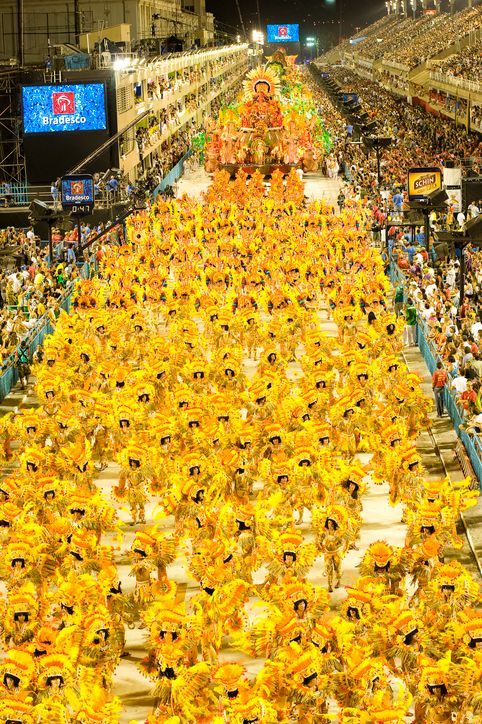 An elevated view of a nighttime parade with a large group of performers in elaborate yellow costumes and headdresses.