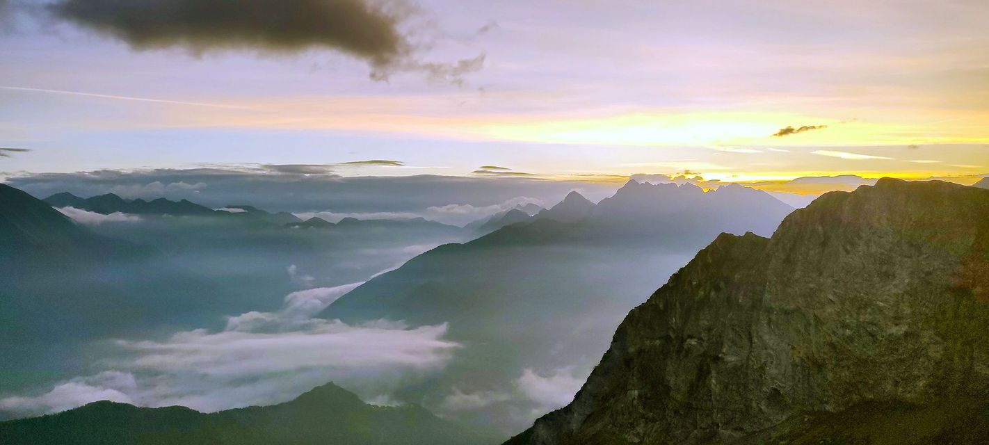 Una vista panoramica di una catena montuosa con cime che emergono dalle nuvole sotto un cielo all'alba.