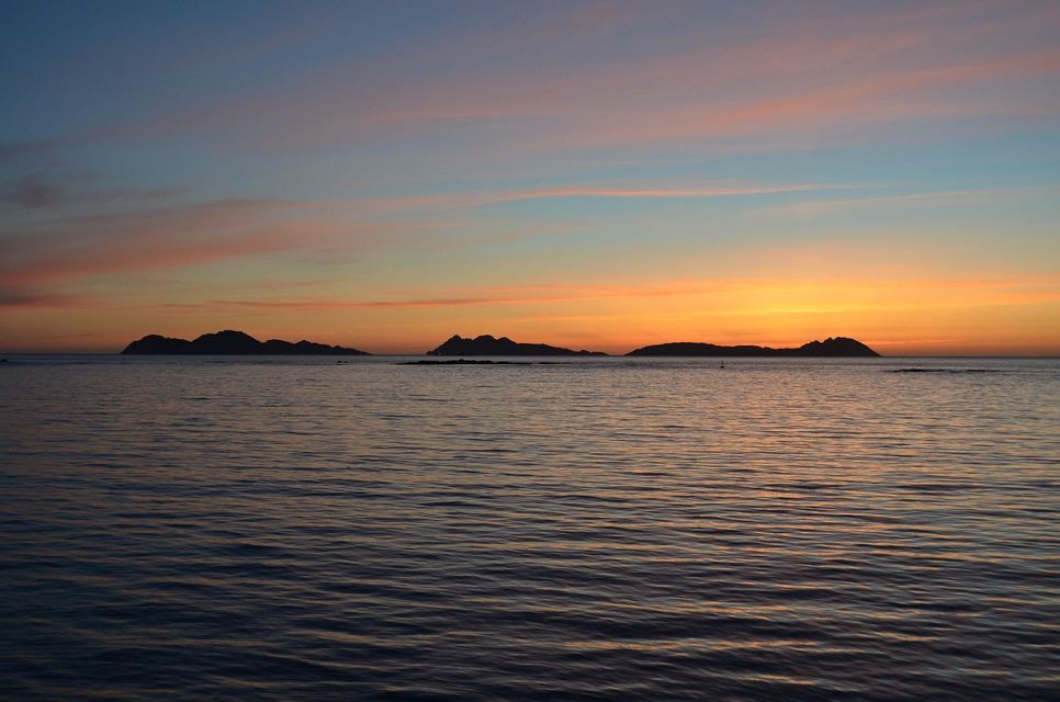 Islas distantes se siluetean contra un cielo de atardecer colorido sobre el mar en calma y ondulante.