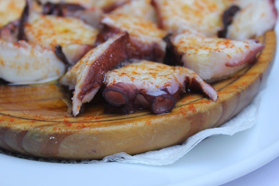 Primer plano de pulpo en rodajas sazonado con pimentón y aceite de oliva, servido en un plato redondo de madera tradicional.