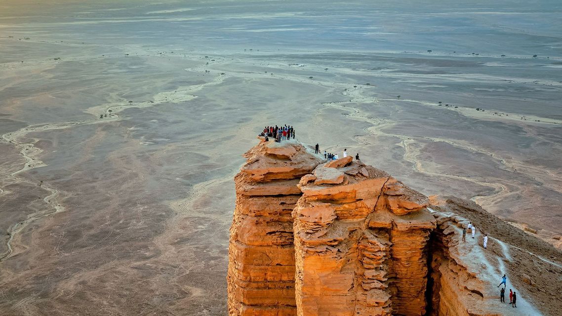 Un viaggio di gruppo WeRoad si trova sul bordo di un'alta scogliera di roccia rossa, affacciato su una vasta pianura desertica.