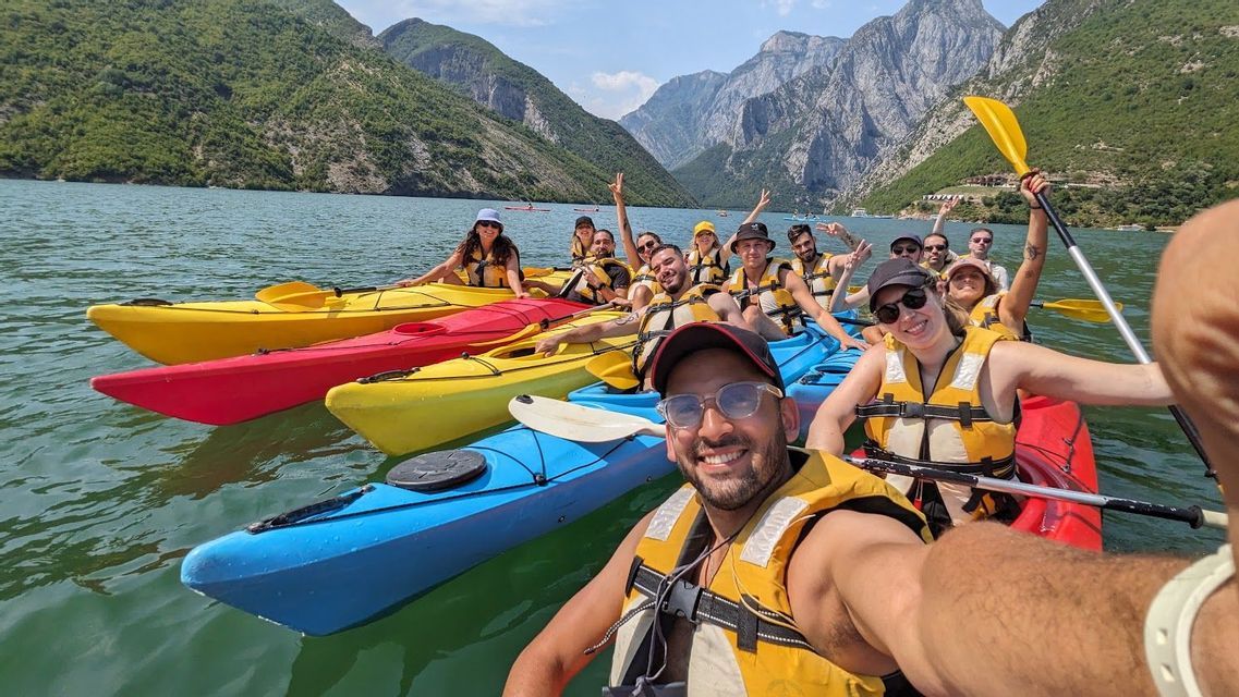 Un grupo de WeRoad se toma una selfie mientras hacen kayak en un gran lago rodeado de montañas.