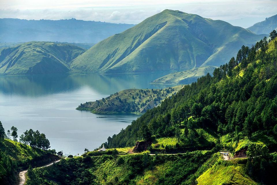 Una vista panoramica su una strada tortuosa mostra un grande lago circondato da rigogliose montagne verdi e foreste.