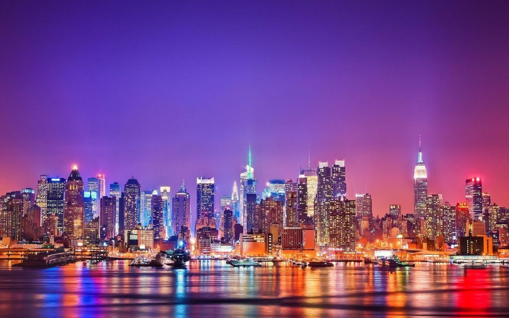 Una vista panoramica dello skyline di una città illuminato da luci vivaci di notte, con riflessi sulla superficie dell'acqua