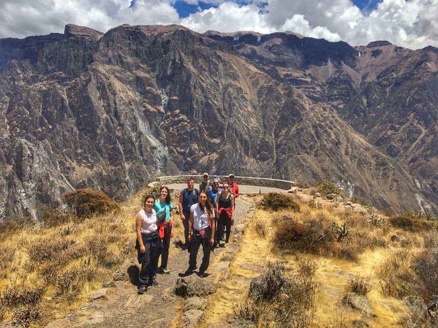 Un grupo de WeRoad sonríe para la cámara en un sendero de montaña polvoriento, con un gran cañón rocoso que se extiende detrás de ellos.