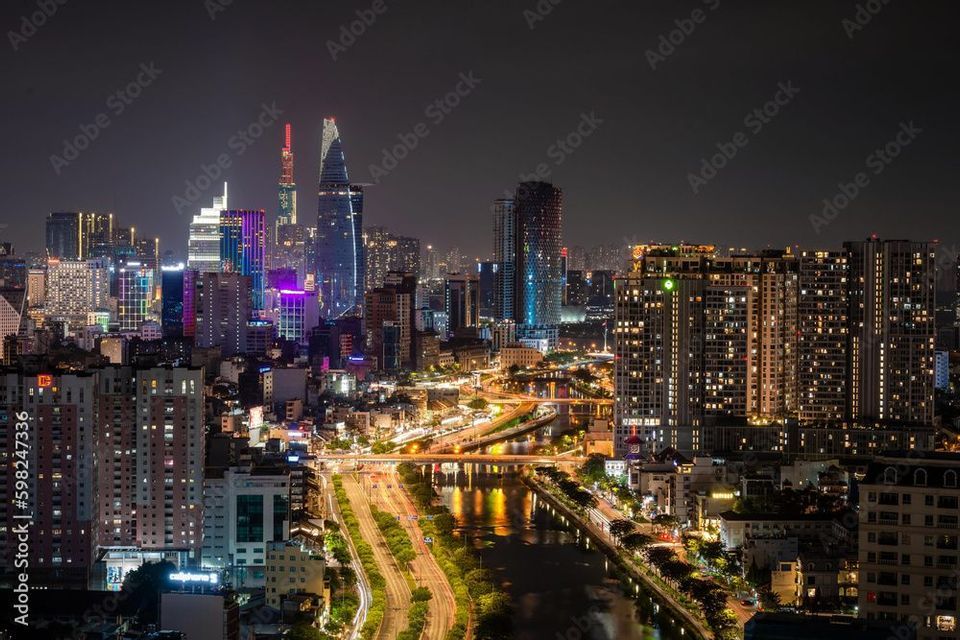 Una vista aerea di una città illuminata di notte, con grattacieli moderni e traffico sulle autostrade lungo un fiume.
