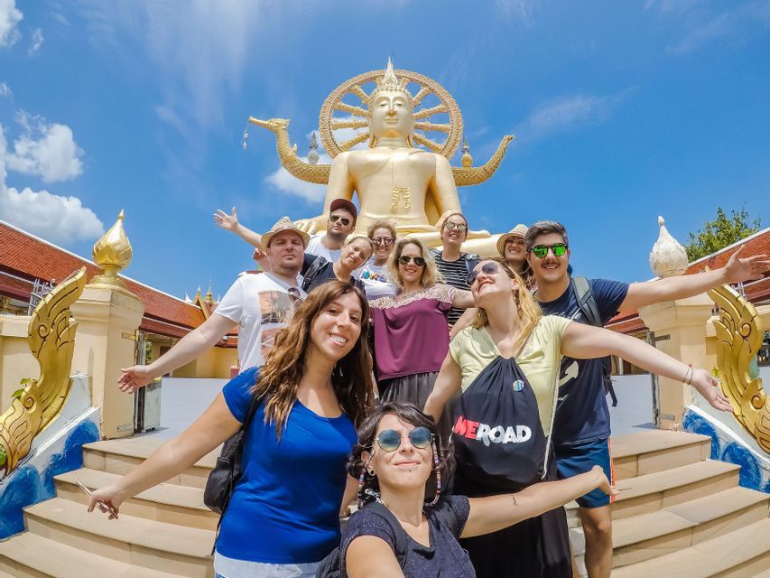 Un viaggio di gruppo WeRoad in posa per una foto sulle scale del tempio di fronte a una grande statua dorata di Buddha sotto un cielo blu.