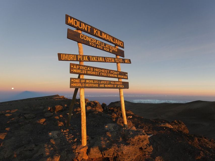 The summit sign at Uhuru Peak on Mount Kilimanjaro, standing on rocky ground at sunrise.