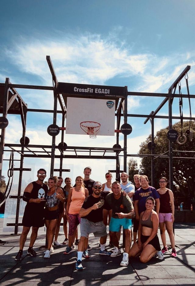 Un gruppo WeRoad in viaggio che posa per una foto di gruppo presso una struttura CrossFit all'aperto sotto un cielo azzurro.