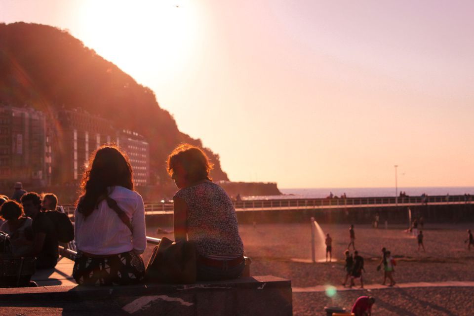 Two women from a WeRoad group trip watch the sunset over a busy beach from a viewpoint.