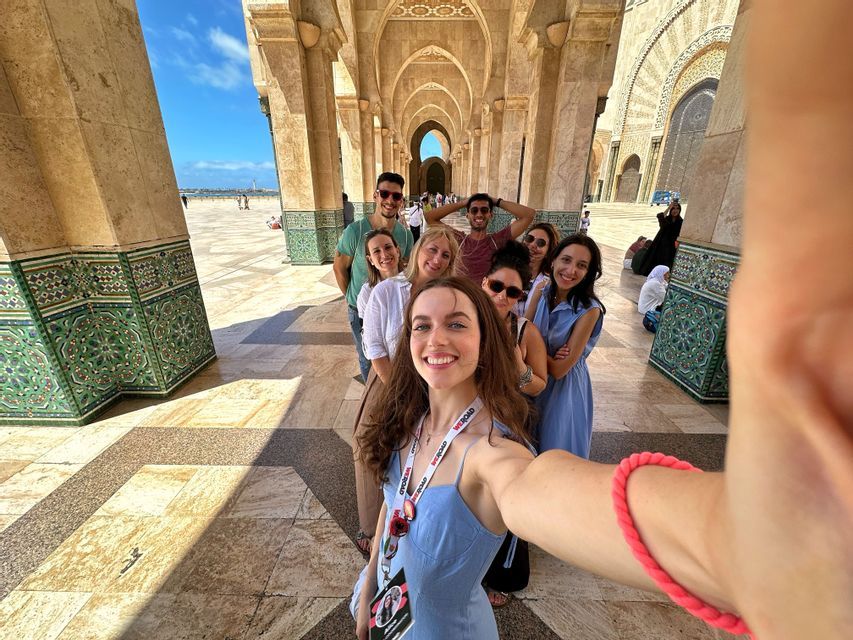 Un groupe WeRoad sourit et pose pour un selfie en faisant la queue sous une colonnade arquée ornée.